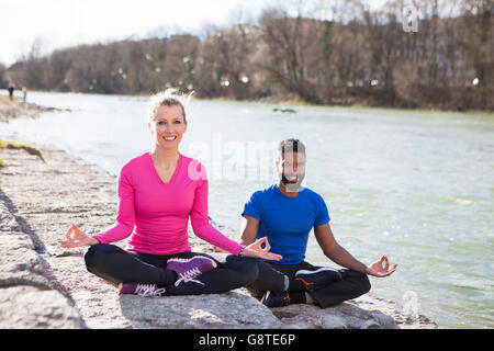 Jeune couple practicing yoga par le Riverside Banque D'Images