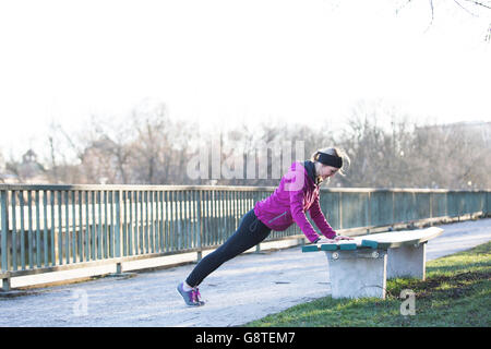 Young woman doing push-ups au banc de parc en ville Banque D'Images