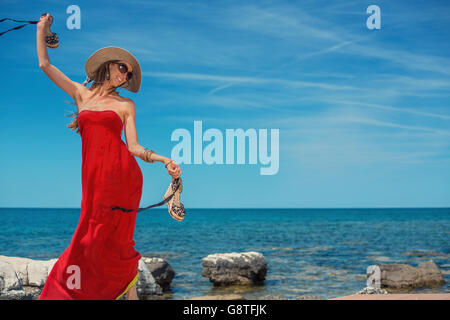 Belle femme en robe d'été rouge danser au bord de la mer Banque D'Images