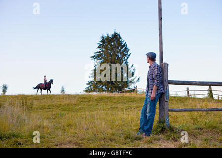 L'équitation femme in rural pasture tandis que l'homme est à regarder Banque D'Images