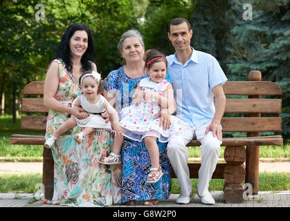 Grande famille s'asseoir sur le banc de bois du parc de la ville, saison d'été, enfant, parent et grand-mère, petit groupe de cinq personnes Banque D'Images