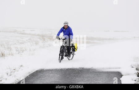 Un cycliste sur les routes au-dessus de Swaledale dans les Yorkshire Dales, alors que le jour de mai, l'escapade de vacances en banque est sur le point d'être entassée par les conditions hivernales, et ceux qui se sont mis en route après le travail le vendredi sont avertis de s'attendre à la grêle, au traîneau et à la neige. Banque D'Images