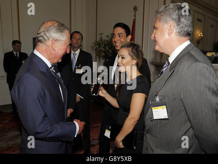 Le Prince de Galles (à gauche) réagit alors que la présentatrice de télévision canadienne Melissa Grelo (deuxième à droite) lui montre une image d'elle-même posant pour une photographie avec le Prince Harry, lors d'une visite de la Maison du Canada à Trafalgar Square, à Londres, pour voir les travaux de restauration récents. Banque D'Images