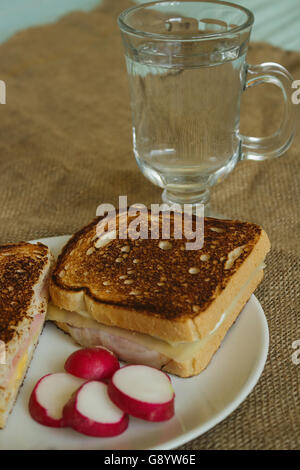 Toast avec du fromage et du bacon sur une plaque blanche avec des radis tranchés dans un verre de soda Banque D'Images