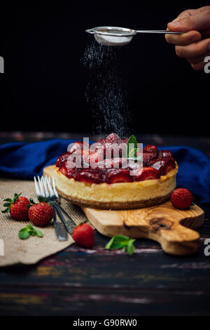 Le tamisage à la main du sucre en poudre sur le gâteau au fromage aux fraises avec un plateau de la crépine. Banque D'Images