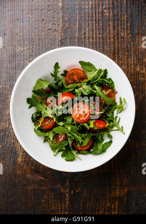 Avec salade de tomates cerises et de la roquette dans un bol blanc sur fond de bois Banque D'Images