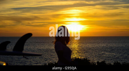 Surf sur un toit de voiture par la mer au coucher du soleil Banque D'Images