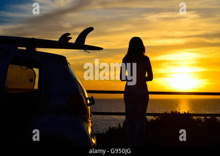 Surf sur un toit de voiture par la mer au coucher du soleil Banque D'Images