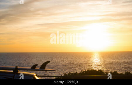 Surf sur un toit de voiture par la mer au coucher du soleil Banque D'Images