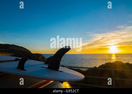Surf sur un toit de voiture par la mer au coucher du soleil Banque D'Images
