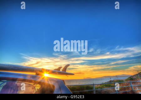 Surf sur un toit de voiture par la mer au coucher du soleil Banque D'Images
