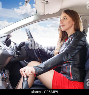 Belle jeune femme volant de la conduite d'une voiture. Confiant smiling dame en robe rouge à la conduite d'une voiture Banque D'Images