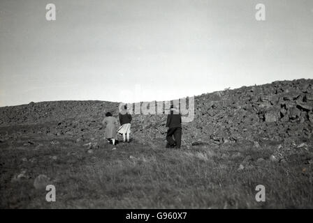 Années 1950, historique, pour une marche rapide, nous voyons ici un vieux monsieur en costume et chapeau et deux, dame et de la jeune fille à monter une colline rocheuse, Grassy Lake district, en Angleterre. Banque D'Images