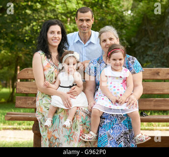 Grande famille s'asseoir sur le banc de bois du parc de la ville, saison d'été, enfant, parent et grand-mère, groupe de 5 personnes Banque D'Images