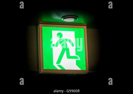 Symbole de sortie d'urgence dans le vert brillant fond noir Banque D'Images