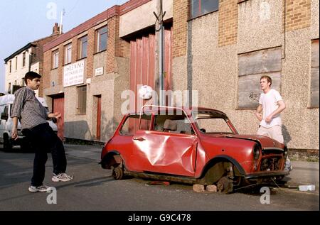 Football.Deux lads utilisant un ancien Mini abandonné pour ajouter un peu d'épices à un kickabout dans les Meadows, ville intérieure de Nottingham Banque D'Images