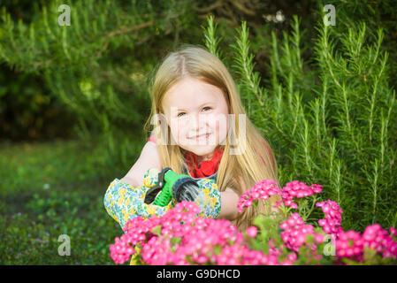 Belle fille blonde arrosage des fleurs, pelouse sur une belle journée ensoleillée en face de la maison. Banque D'Images