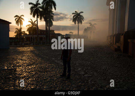 Un homme portant un chapeau de cow-boy s'élève dans un nuage d'insecticide moustiques au coucher du soleil sur la Plaza Mayor de Cuba Trinidad Banque D'Images