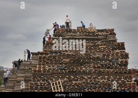 Les jeunes fidèles construisent un feu de camp sur la route Shankill à Belfast. Il s'agit de l'un des plus grands feux de joie à être incendié ce soir en Irlande du Nord, ce qui indique le début de la plus grande journée de marche dans le calendrier de l'ordre Orange. Banque D'Images