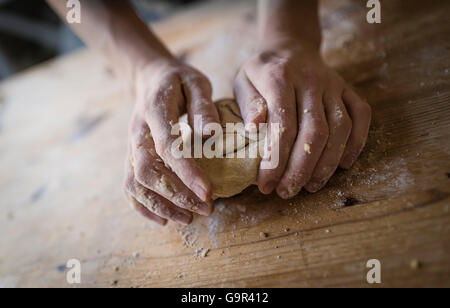 Close-up de deux mains fortes d'un baker que sont la pâte à pétrir manuellement sur une table de cuisine en bois, Banque D'Images