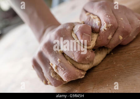 Close-up de deux mains fortes d'un baker que sont la pâte à pétrir manuellement sur une table de cuisine en bois, Banque D'Images