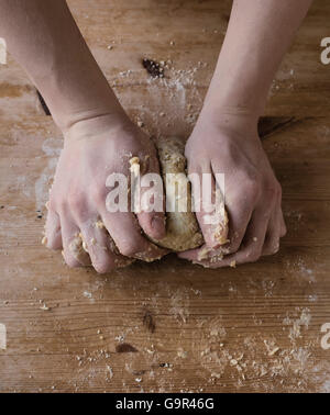 Close-up de deux mains fortes d'un baker que sont la pâte à pétrir manuellement sur une table de cuisine en bois, Banque D'Images