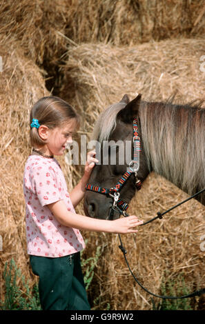 Fille avec poney Shetland / Shetty, paille, bridle Banque D'Images