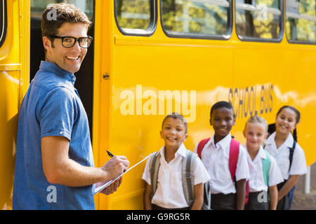 Smiling teacher mise à jour vérifier liste des enfants lors de l'entrée in bus Banque D'Images