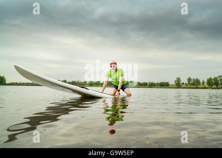 Senior male pagayeur sur un paddleboard, Lake dans le nord du Colorado, clody matin d'été Banque D'Images