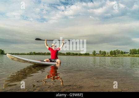 Senior male pagayeur assis sur un paddleboard, Lake dans le nord du Colorado avec un décor au début de l'été Banque D'Images