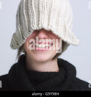 Jeune fille portant un bonnet de laine, couvrant les yeux, smiling Banque D'Images