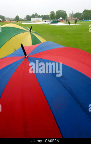 Les fans regardent de sous leur parapluie que le personnel du terrain remplacent les couvertures sur le terrain avant le début du match de Liverpool Victoria County Championship Division Two entre Leicestershire et le match de Notinghamshire à l'Oakham School. Banque D'Images