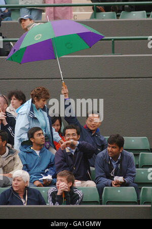 Un fan tient son parapluie alors que la pluie retarde le match entre Justine Henin en Belgique et Jorgelina Cravero en Argentine sur le court One pendant le championnat de tennis de pelouse de toute l'Angleterre à Wimbledon. Banque D'Images