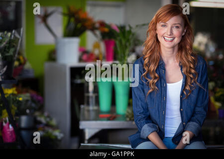 Happy female florist sitting on table in flower shop Banque D'Images