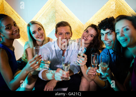 Group of smiling friends sitting on sofa et avoir un verres de champagne Banque D'Images