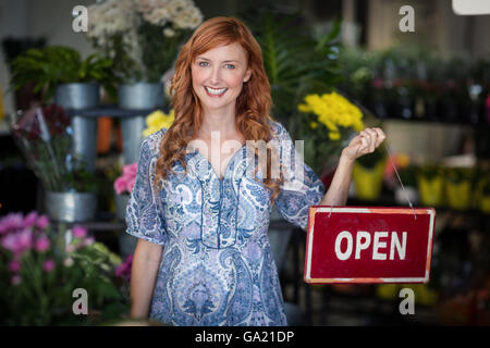 Les fleuristes Smiling holding open sign placard in flower shop Banque D'Images