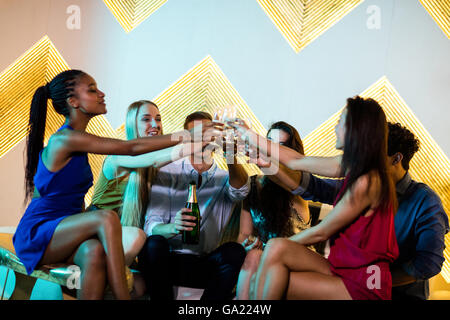 Group of smiling friends sitting on sofa et un grillage verres de champagne Banque D'Images