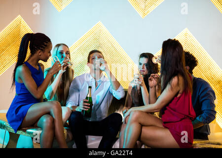 Group of smiling friends sitting on sofa et avoir un verres de champagne Banque D'Images