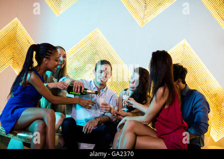 Group of smiling friends sitting on sofa et avoir un verre de champagne Banque D'Images