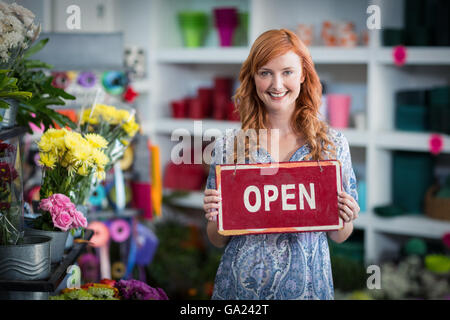 Les fleuristes Smiling holding open sign placard in flower shop Banque D'Images