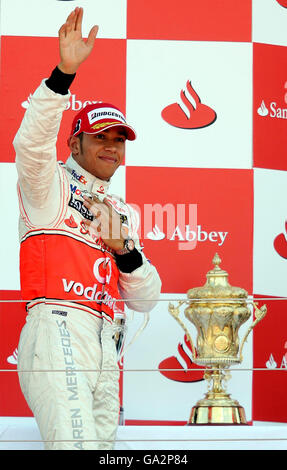 Lewis Hamilton, en Grande-Bretagne, se hisse devant la foule lorsqu'il passe le trophée des gagnants sur le podium au Grand Prix britannique de Silverstone, dans le Northamptonshire. Banque D'Images