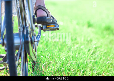 Le pied sur la pédale vélo femme sur l'herbe verte libre Banque D'Images