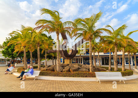 Port de plaisance de Puerto Calero, LANZAROTE ISLAND - 12 jan 2015 : place avec des palmiers et des gens assis sur un banc dans le port de Puerto Calero construit dans le style des Caraïbes. C'est un port de plaisance moderne. Banque D'Images