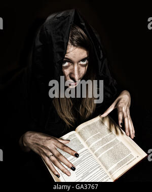 Jolie sorcière jette des sorts du livre ancien épais aux chandelles sur un fond sombre Banque D'Images
