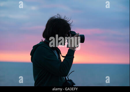 Une silhouette d'un photographe professionnel qui prend une photo avec un appareil photo DSLR against a sunset Banque D'Images