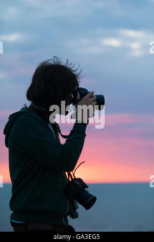 Une silhouette d'un photographe professionnel qui prend une photo avec un appareil photo DSLR against a sunset Banque D'Images