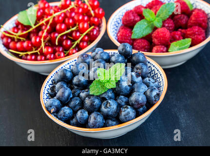 Frais sain bleuets, framboises et groseilles rouges dans des bols rustiques de feuilles de menthe Banque D'Images