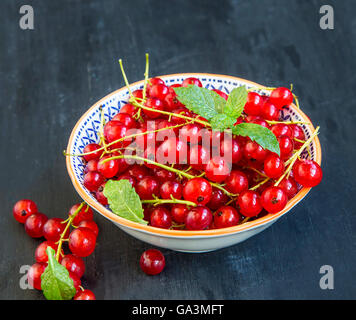 Groseilles fraîches rouge dans un bol rustique avec des feuilles de menthe Banque D'Images