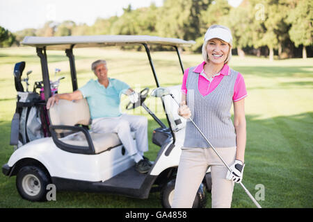 Smiling mature woman standing by man en voiturette de golf Banque D'Images