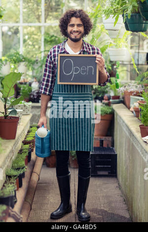 Jardinier mâle holding open sign plaque et de l'arrosoir Banque D'Images